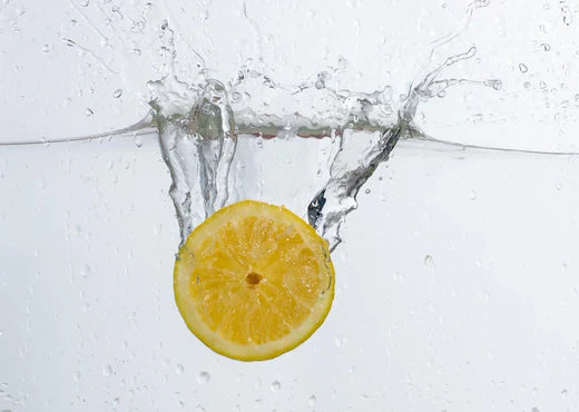 Mitad de un limón cayendo en agua, creando un efecto de salpicadura cristalina y refrescante.