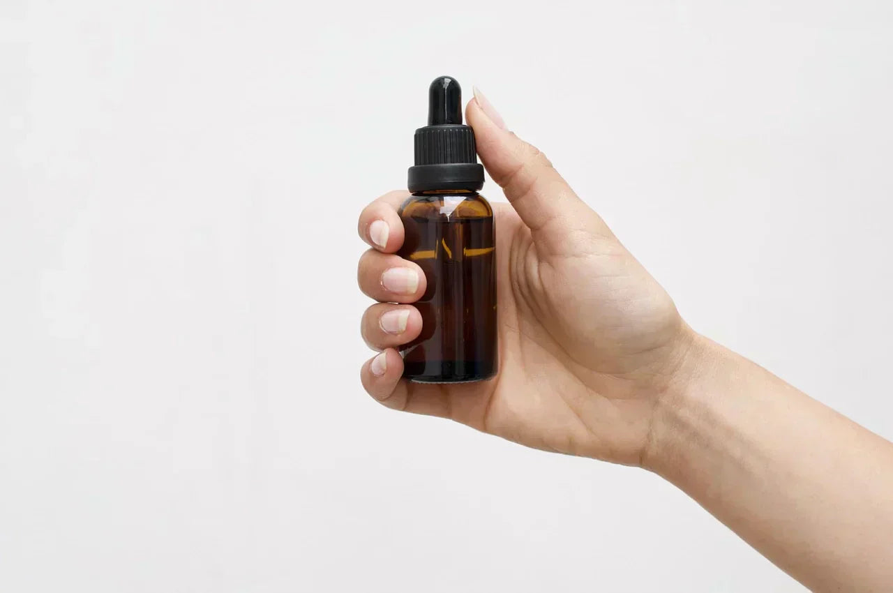 Mano sosteniendo un frasco de vidrio ámbar con gotero, utilizado para almacenar sueros o aceites cosméticos.