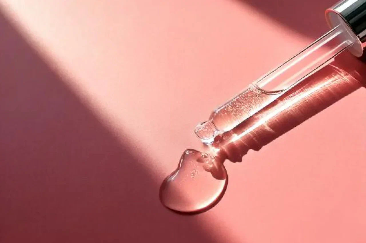 Primer plano de una pipeta con suero transparente sobre una superficie rosa, con reflejos de luz y sombras suaves. Imagen generada con inteligencia artificial.